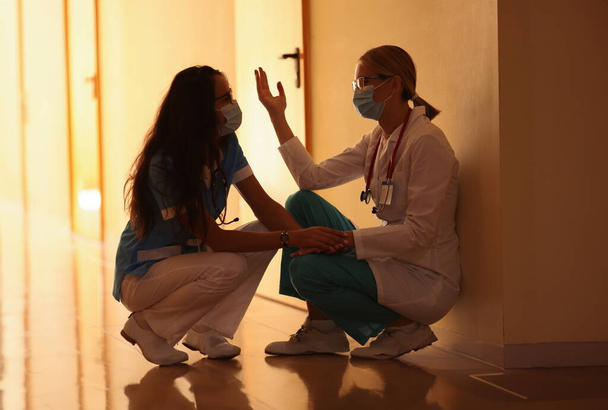 Két frusztrált orvos ül a kórház folyosóján. Orvosok a coronavirus pandémia koncepciójában - Fotó, kép