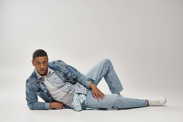 привлекательный эмоциональный африканский американец в стильной джинсовой одежде позирует в движении, концепция моды - Фото, изображение