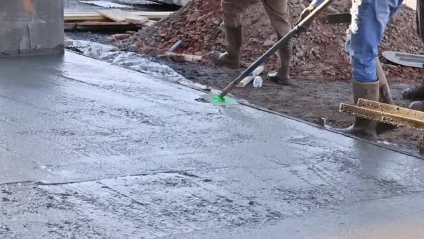 There is worker holding a steel fresno concrete trowel against freshly poured concrete as he smooths the plastering of new sidewalks in construction site - Filmati, video