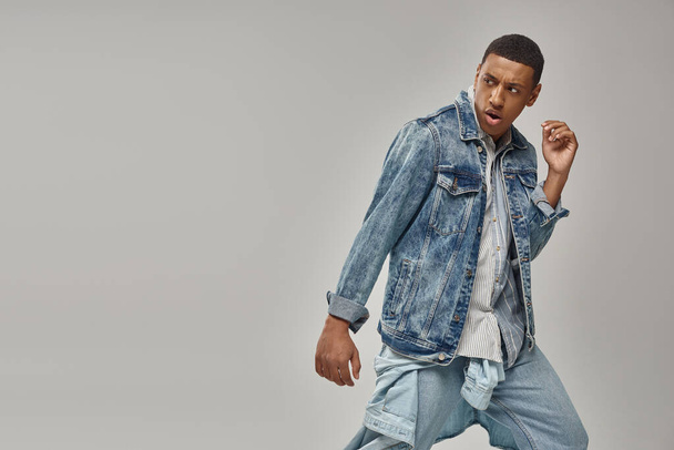 attractive emotional african american man in stylish denim outfit posing in motion, fashion concept - Photo, Image