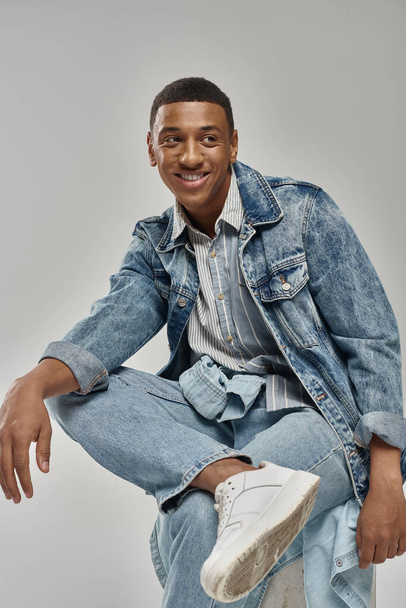 good looking african american male model in denim outfit sitting on white cube, fashion concept - Foto, Bild