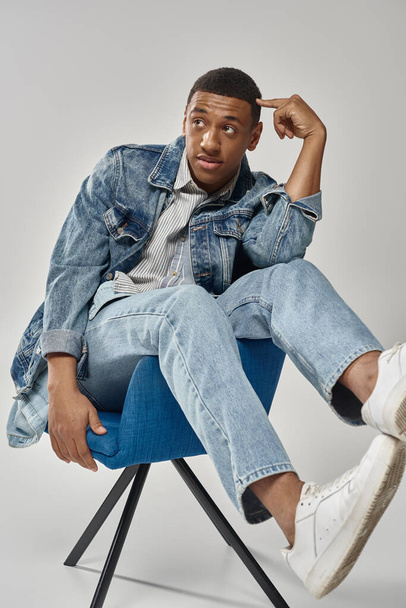 surpreso homem americano africano em roupa jeans elegante sentado na cadeira azul, conceito de moda - Foto, Imagem