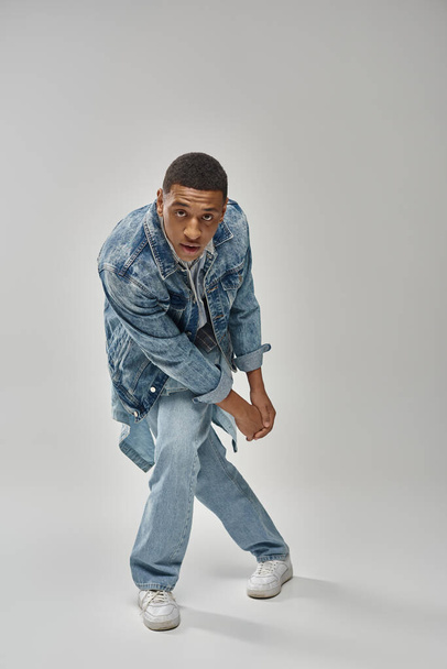 привабливий емоційний афроамериканський чоловік у стильному джинсовому вбранні, що жестикулює живим, концепція моди - Фото, зображення