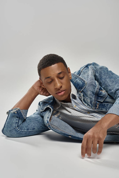 gut aussehender junger afrikanisch-amerikanischer Mann im trendigen Jeans-Outfit auf dem Boden liegend, Modekonzept - Foto, Bild