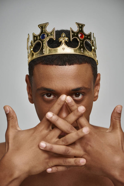 atractivo hombre afroamericano en la corona de oro posando en topless con las manos cerca de la cara, concepto de moda - Foto, imagen