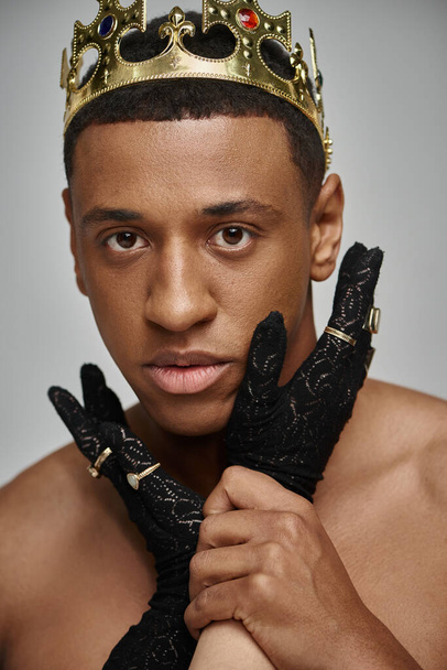 main féminine en gant noir avec anneaux près du visage de l'homme afro-américain torse nu avec couronne - Photo, image