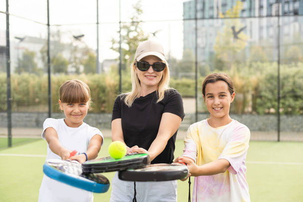 Young sporty woman with children playing padel game in court on sunny day. High quality photo - Photo, Image