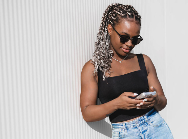 Портрет молодої красивої афроамериканки з довгими косами з телефоном в руках на білому тлі - Фото, зображення