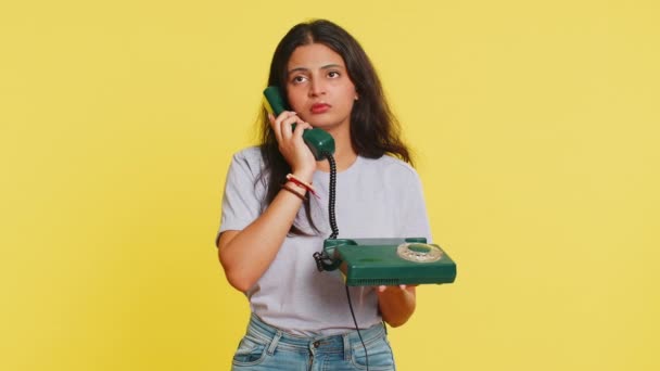 Tired bored Indian woman talking on wired vintage telephone of 80s, fooling, making silly faces, exhausted of tedious story, not interested in communication talk. Arabian girl on yellow background - Footage, Video