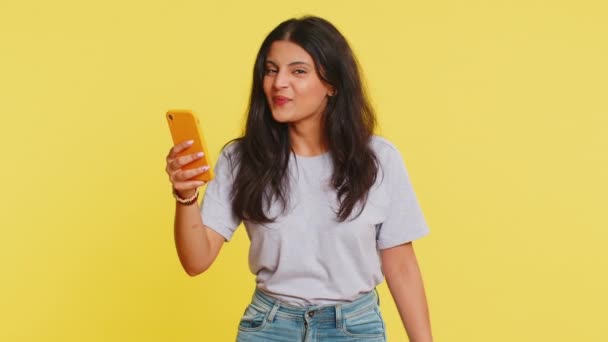 Indyjska kobieta szuka smartfona wyświetlacza szczerze radując zwycięstwo, odbieranie banknotów gotówkowych dolarów świętując sukces zwycięstwa grać w loterię. Szczęśliwy bogaty arabski dziewczyna na żółtym tle - Materiał filmowy, wideo
