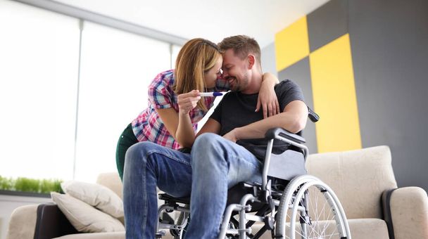 Radosna kobieta i mężczyzna na wózku inwalidzkim z testem ciążowym. Pierwsze emocje przyszłej koncepcji rodziców - Zdjęcie, obraz