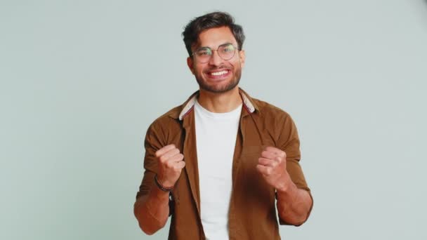 Happy joyful Indian man celebrating success victory, winning birthday, lottery jackpot goal achievement play game good positive news, triumph. Young Arabian guy isolated on gray studio background - Footage, Video