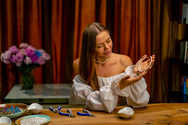 hermosa joven costurera está haciendo buscando hecho collar de perlas artesanía fabricación de joyas hobby trabajo en casa - Foto, imagen
