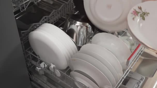 Egy férfi koszos tányérokat tesz egy mosogatógépbe, tele piszkos edényekkel. Takarítás a konyhában. - Felvétel, videó