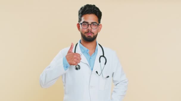 Όπως. Ινδός νεαρός καρδιολόγος γιατρός σηκώνει τους αντίχειρες επάνω συμφωνεί, δίνει θετική απάντηση καλή ιδέα ανατροφοδότηση, γιορτάζει τη νίκη επιτυχία. Αραβικός φαρμακοποιός φαρμακοποιός τύπος απομονωμένος σε μπεζ φόντο - Πλάνα, βίντεο