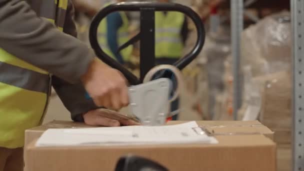 Tunnistamattoman varastotyöntekijän keskiosa, joka käyttää teippiä pahvilaatikon pakkaamiseen ja laskutuspaperin allekirjoittamiseen, paketin valmisteluun kuljetusta ja lähettämistä varten - Materiaali, video