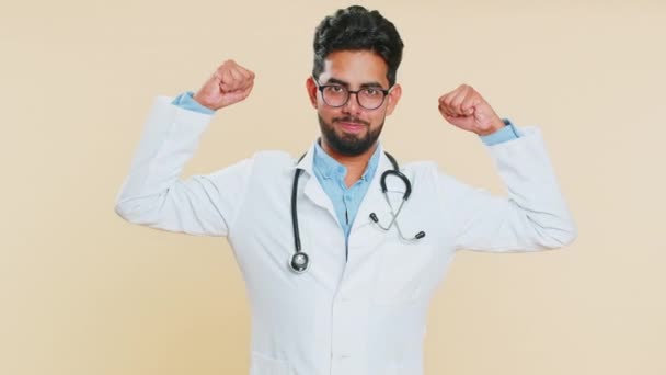 Я сильний. Індійський молодий лікар кардіолог демонструє біцепс і впевнено відчуває силу боротьби за енергію прав, щоб отримати перемогу в успіху. Арабський аптекарець на бежевому фоні - Кадри, відео