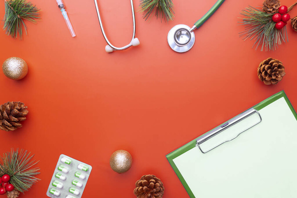 Χριστουγεννιάτικη ευχετήρια κάρτα για ιατρική και υγειονομική περίθαλψη έννοια. Χριστουγεννιάτικο πανό με γιορτινή διακόσμηση, ιατρικό στηθοσκόπιο, σύριγγα και χάπια σε κόκκινο φόντο. - Φωτογραφία, εικόνα