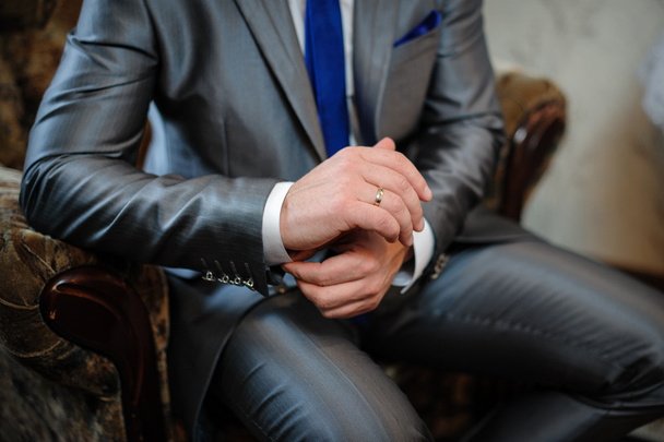 man in een pak zittend in een stoel en brengt cufflinks - Foto, afbeelding