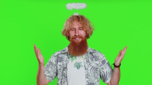 Portrait of smiling shy angelic young caucasian man with angel halo nimb over head flirting, looking at camera, positive love emotions celebrating holiday. Redhead bearded guy on chroma key background - Footage, Video