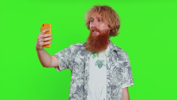 Щасливий молодий кавказький блогер бере портрет селфі на смартфон, спілкуючись записом відеодзвінків в Інтернеті з підписками на соціальні мережі. Рудий бородатий хлопець ізольований на фоні ключа зеленої хроми - Кадри, відео