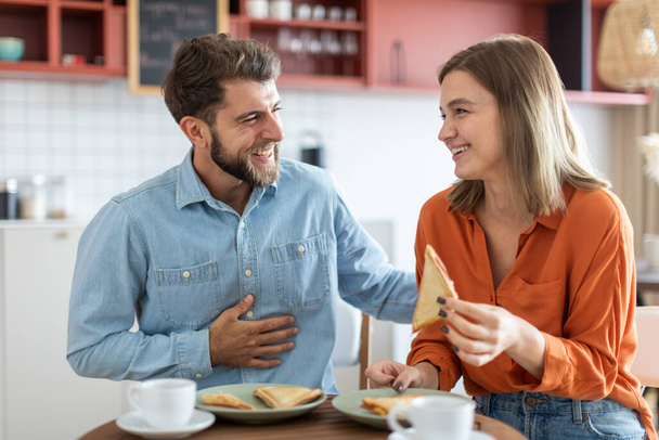 Felices amigos caucásicos hombre y mujer sentados en la cafetería y hablando, tomando un aperitivo con sándwiches y tomando café - Foto, imagen