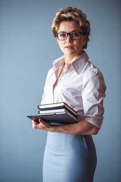 Belle psychothérapeute en costume et lunettes tient des livres et regarde la caméra, sur fond gris
 - Photo, image