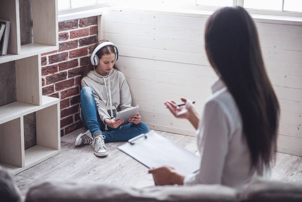 Tizenéves lány a pszichoterapeuta. Orvos a jegyzetelést, míg a lány ül a sarokban, a padlón fejhallgató - Fotó, kép