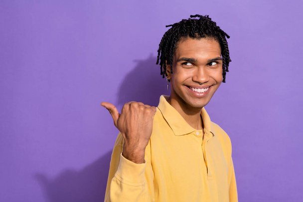 Photo of toothy beaming person with cornrows wear stylish shirt directing look at promo empty space isolated on purple color background. - Фото, зображення