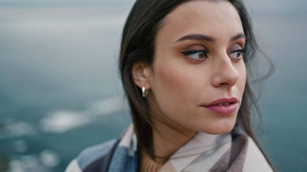 Portrait of beautiful young woman standing in front gray gloomy seascape. Relaxed tranquil girl looking camera relaxing on cloudy nature close up. Attractive dark haired lady posing on sea shore alone - Photo, Image
