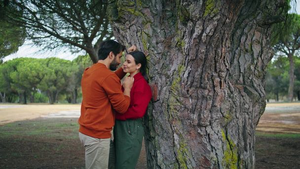 Romantic young couple standing in forest spending weekend together. Loving two people leaning on wide tree enjoying happy date. Tender beautiful pair tourists relaxing on nature feeling closeness love - Photo, Image
