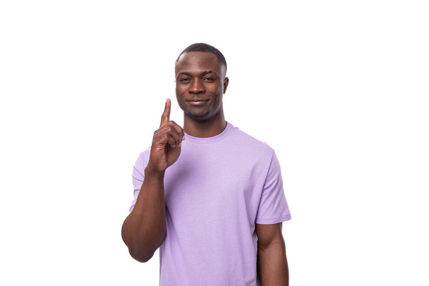 νεαρός επιτυχημένος Αμερικανός άνδρας ντυμένος με ένα ελαφρύ λιλά t-shirt σε λευκό φόντο με χώρο αντιγραφής. - Φωτογραφία, εικόνα