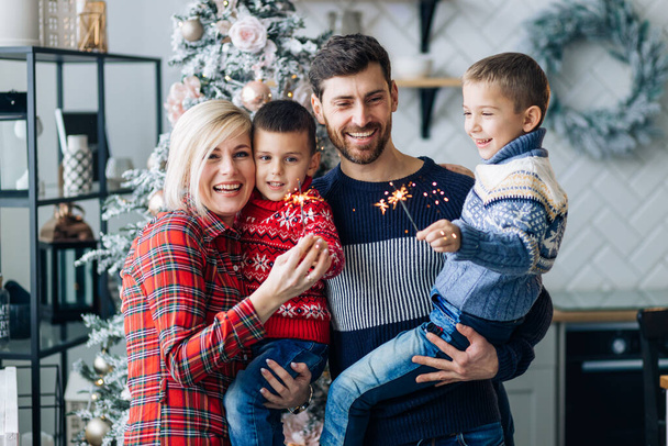 Madre, padre, dos hijos posando con bengalas durante la Navidad en casa con el telón de fondo de decoraciones - Foto, Imagen