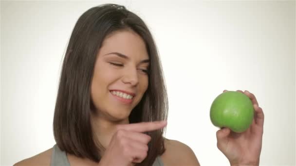 女の子は緑のリンゴ、スポーツの概念と健康的な食事を保持しています。健康的なフィットネスと食事のライフスタイルの概念。彼女のよく訓練された体を示すフィットネススポーティな女性, 白い背景の上に隔離. - 映像、動画