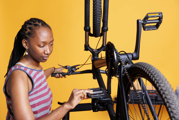 Odhodlaná Afroameričanka viděla, jak kontroluje poškození motorky. S bystrým okem pro detail, mladá černoška kontroluje cyklistické pedály a brzdy zajišťující hladké a efektivní venkovní cyklistiku. - Fotografie, Obrázek