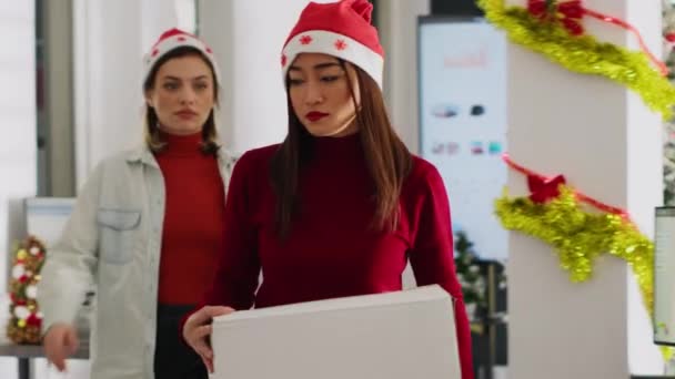 Közelkép egy szomorú munkásról ünnepi díszítésű irodai cuccokban az utolsó munkanapon. Karácsonyi kalapot viselő ázsiai nő, akit kirúgnak a munkából a karácsonyi ünnepek előtt, elmegy - Felvétel, videó