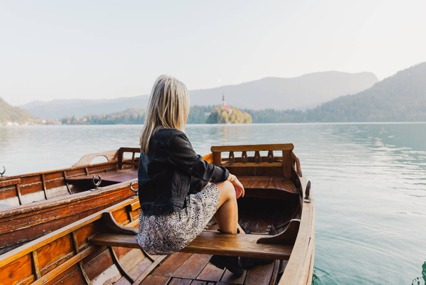 Una donna seduta su una barca osserva il lago durante una giornata autunnale, foto da dietro - Foto, immagini