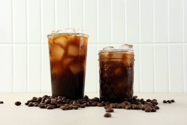 Δύο ποτήρι παγωμένο μαύρο καφέ με φασόλι καφέ σε λευκό φόντο, φρέσκο ποτό το καλοκαίρι - Φωτογραφία, εικόνα