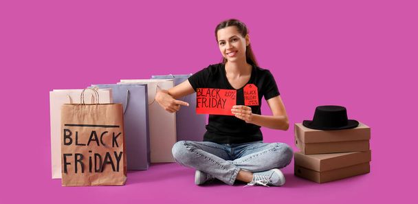 Mujer joven con bolsas de compras y cajas de cartón sobre fondo magenta. Viernes Negro venta - Foto, Imagen