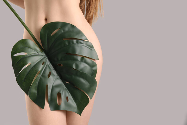 Γυμνή νεαρή γυναίκα με τροπικό φύλλο σε ανοιχτό φόντο. Έννοια της επιληψίας - Φωτογραφία, εικόνα
