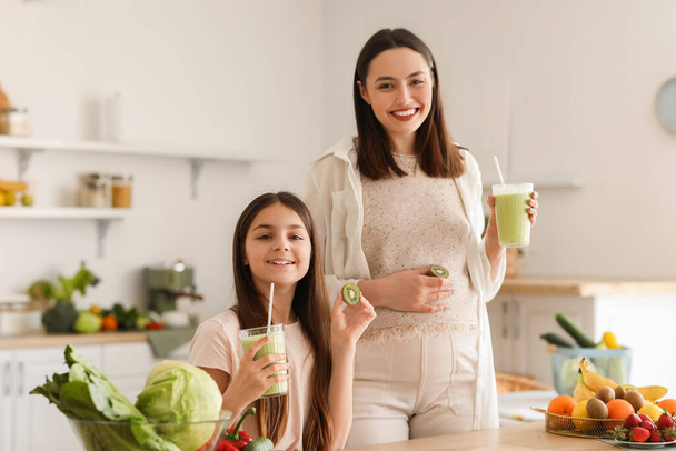 Petite fille avec sa mère enceinte buvant du smoothie vert dans la cuisine - Photo, image