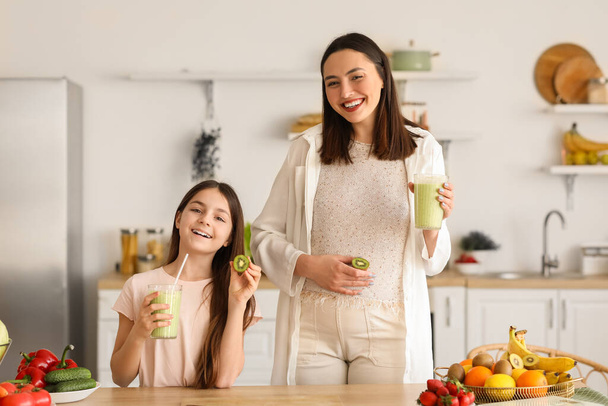 klein meisje met haar zwanger moeder drinken groen smoothie in keuken - Foto, afbeelding
