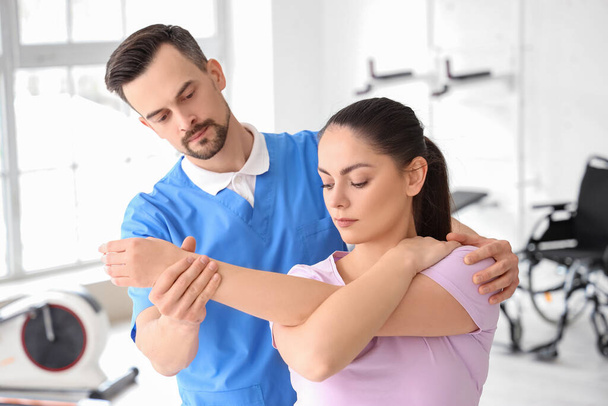 Fisioterapeuta masculino trabajando con una mujer joven en un centro de rehabilitación - Foto, Imagen