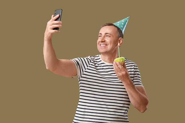 Uomo maturo con torta di compleanno scattare selfie su sfondo verde - Foto, immagini