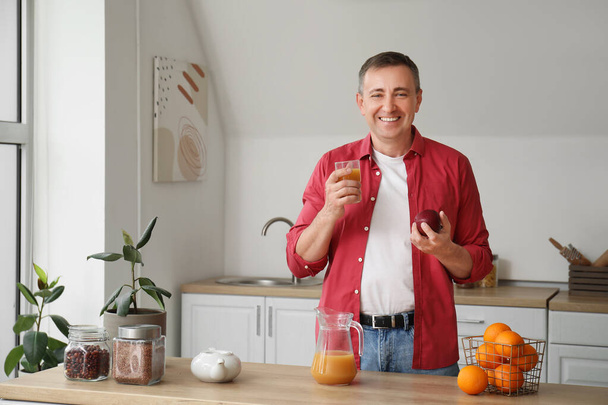 Homme mûr avec un verre de jus d'orange et de pomme dans la cuisine - Photo, image