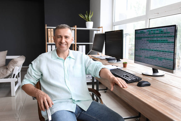 Mature male programmer sitting in light office at his workplace - Photo, Image