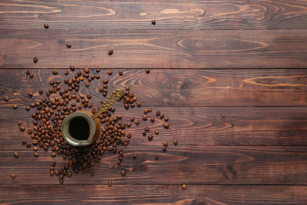 Café en cezve con granos dispersos sobre fondo de madera marrón - Foto, imagen