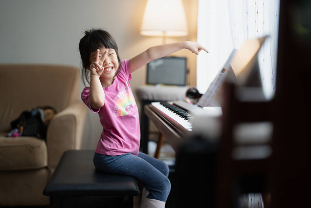 Счастливая азиатская девочка, подающая пальцы рядом с пианино - выражение музыкальной радости - Фото, изображение