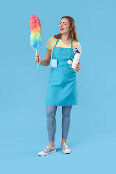 Young woman with bottle of detergent and pp-duster on blue background - Photo, Image
