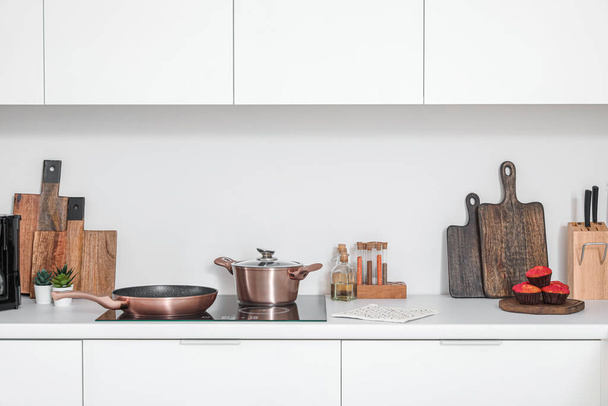 Bancada de cozinha branca com fogão elétrico, frigideira, panela de cozinhar e utensílios - Foto, Imagem